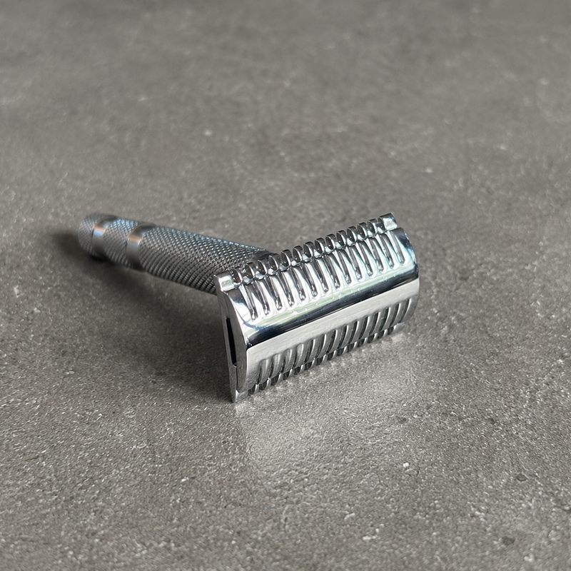 A classic silver stainless steel safety razor with a ribbed metal head and knurled grip, resting on a textured gray surface.